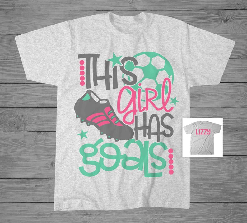May include: Gray t-shirt with a green and pink design that says "This girl has goals". The design includes a soccer ball, a soccer cleat, and stars. The shirt is personalized with the name "Lizzy" on a separate gray t-shirt.
