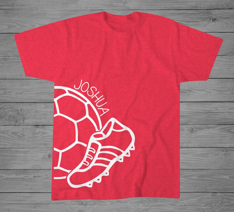 May include: Red t-shirt with a white soccer ball and a white shoe graphic. The text "JOSHUA" is written on the shirt.