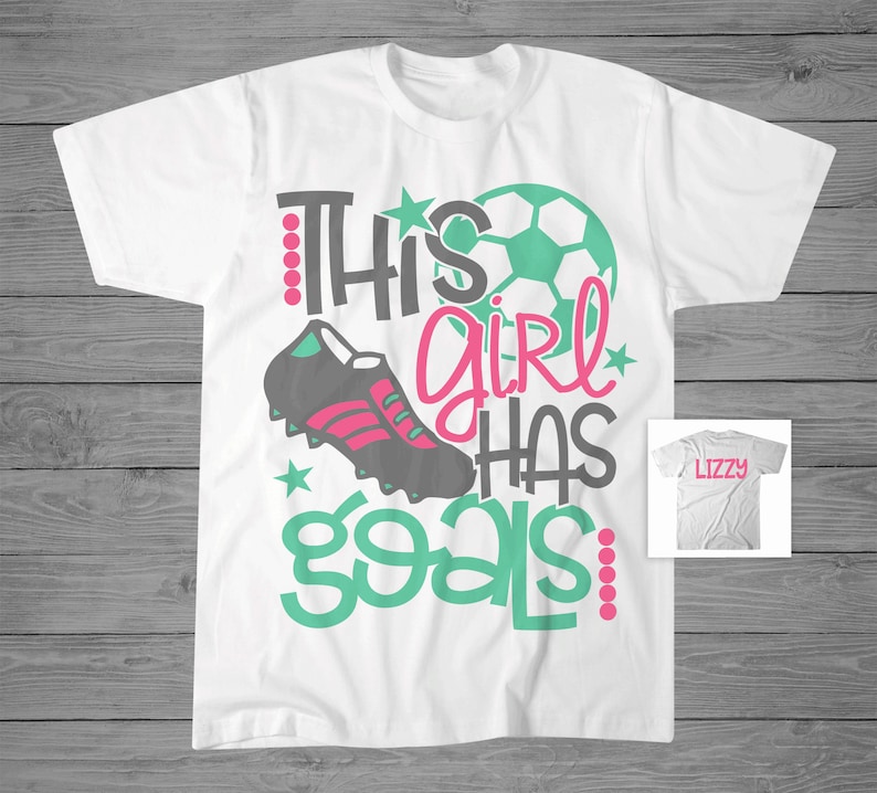 May include: White t-shirt with the text "This girl has goals" in green and pink. A soccer ball and a soccer cleat are also featured on the shirt.