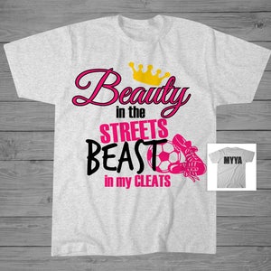 May include: Gray t-shirt with pink text that reads "Beauty in the Streets Beast in my Cleats" with a gold crown above the word "Beauty" and a soccer ball and cleat graphic.