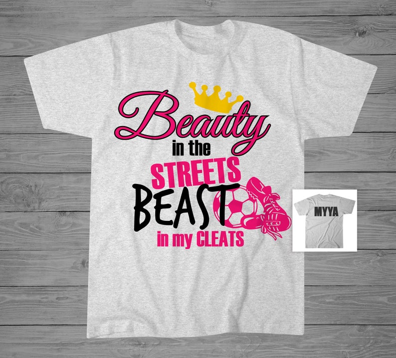 May include: Gray t-shirt with pink text that reads "Beauty in the Streets Beast in my Cleats" with a gold crown above the word "Beauty" and a soccer ball and cleat graphic.