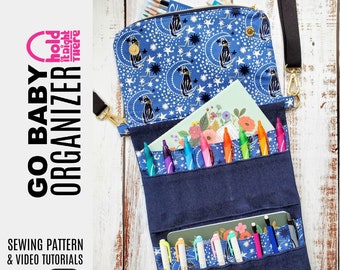 May include: A blue and white fabric organiser with a zipper closure and a black strap. The organiser has multiple pockets and is filled with pens and pencils. The text "Go Baby Organiser" is printed on the left side of the image. The text "Hold it Tight There" is printed on the right side of the image.