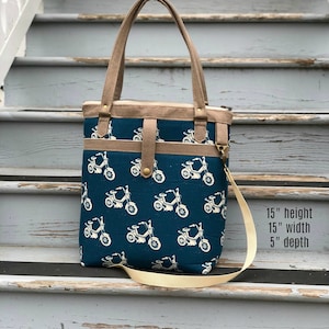 May include: A blue tote bag with a white bicycle pattern. The bag has a brown strap and a zipper closure. The bag is 15 inches high, 15 inches wide, and 5 inches deep.