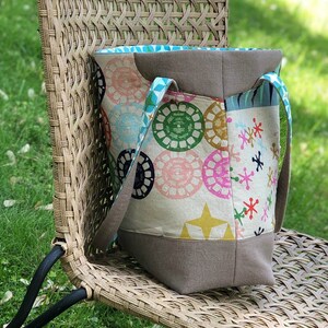 May include: A large, brown and white tote bag with a colorful geometric pattern. The bag has two straps and a zipper closure.