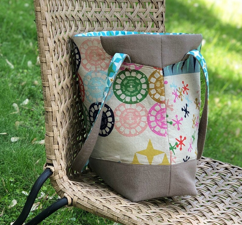 May include: A large, brown and white tote bag with a colorful geometric pattern. The bag has two straps and a zipper closure.
