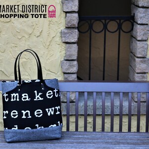 May include: Black and white shopping tote bag with the text "market renew" printed on it. The bag has black leather handles and a gray felt bottom. The bag is sitting on a wooden bench in front of a brick wall.