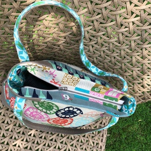 May include: A colorful tote bag with a zipper closure and two handles. The bag is made of fabric with a patchwork design featuring geometric shapes, flowers, and other patterns. The bag is open and the inside is visible.