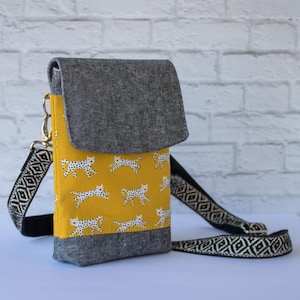 May include: A small yellow crossbody bag with a black and white geometric strap. The bag has a flap closure and is decorated with a repeating pattern of white silhouettes of cats on a yellow background.