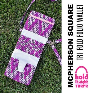 May include: A purple and white patterned tri-fold wallet with a pink zipper and a strap. The wallet is labelled "McPherson Square Tri-Fold Folio Wallet" and has a logo that says "Hold It Right There".
