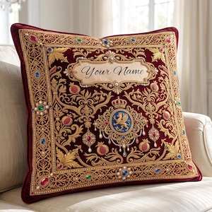 May include: A square velvet throw pillow in deep burgundy featuring intricate gold embroidery, a central blue crest with a griffin, pomegranate motifs, and colorful faux gemstones. The text "Your Name" is printed in a central cream-colored banner.