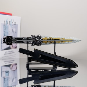 Pode incluir: Uma adaga decorativa com uma lâmina prateada e detalhes dourados, exibida em um suporte preto. A empunhadura é preta com detalhes ornamentados. Uma bainha de couro preta com costura amarela também está incluída.