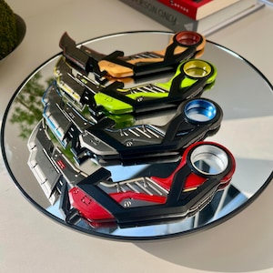 May include: Four futuristic-style letter openers in a variety of colors: orange, green, blue, and red. Each opener has a black handle and a circular opening. The openers are displayed on a reflective surface.