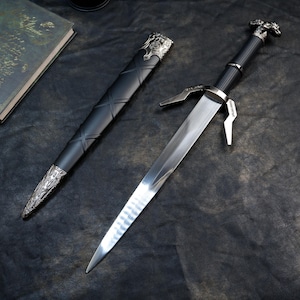May include: A silver and black sword with a decorative handle and crossguard, next to a black sheath with silver accents. The sword's blade is polished and reflects light. The sheath has a crisscross pattern.