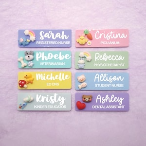 May include: Eight rectangular name badges in pastel colours, each featuring a white name and job title. Decorations include miniature 3D figures like a rainbow, elephant, chick, carrot, dog, bone, cloud, rocket, duck, mushroom, cat, fish, bear, and heart.