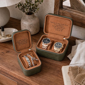 May include: Two dark green rectangular jewellery cases with tan interiors. The smaller case holds a silver chain bracelet and a cross pendant. The larger case holds two metallic wristwatches. Both cases feature engraved messages on the inner lids.