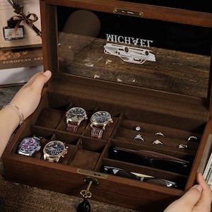 May include: A wooden watch and jewellery box with a glass lid, featuring multiple compartments. The box contains several watches with leather straps, rings, and a pair of sunglasses. The text "WICHYET" is visible on the glass.