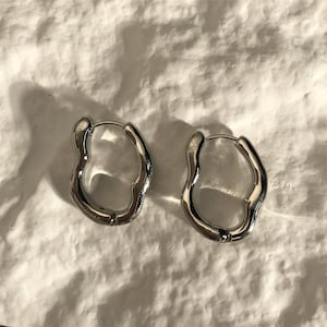 May include: A pair of silver hoop earrings with a wavy, organic shape. The earrings are made of metal and have a polished finish.