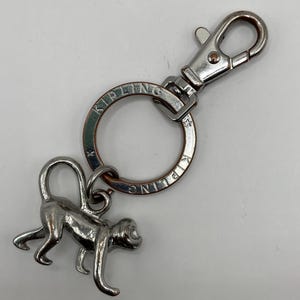 Peut inclure: Porte-clés en forme de singe argenté avec un anneau et un mousqueton argentés. L'anneau porte l'inscription "KIPLING" gravée.