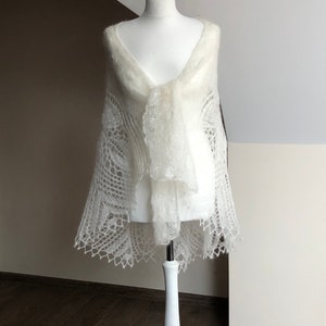 May include: A white knitted shawl with a delicate lace pattern. The shawl is draped over a white mannequin.