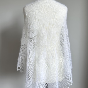 May include: White lace shawl with a delicate floral pattern, draped over a white mannequin.