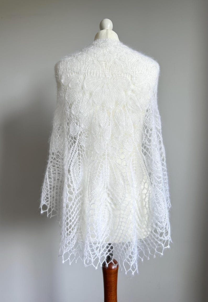 May include: White lace shawl with a delicate floral pattern, draped over a white mannequin.