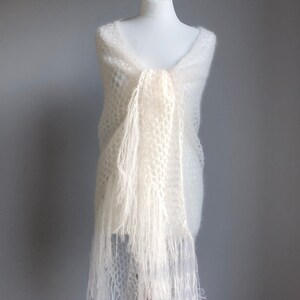 May include: A white crocheted shawl with fringe. The shawl is draped over a white mannequin.
