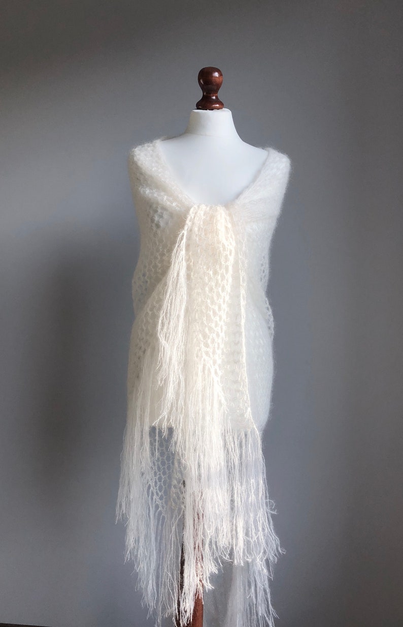 May include: A white crocheted shawl with fringe. The shawl is draped over a white mannequin.