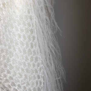 May include: White crocheted shawl with a delicate, lacy pattern and a soft, fluffy texture.