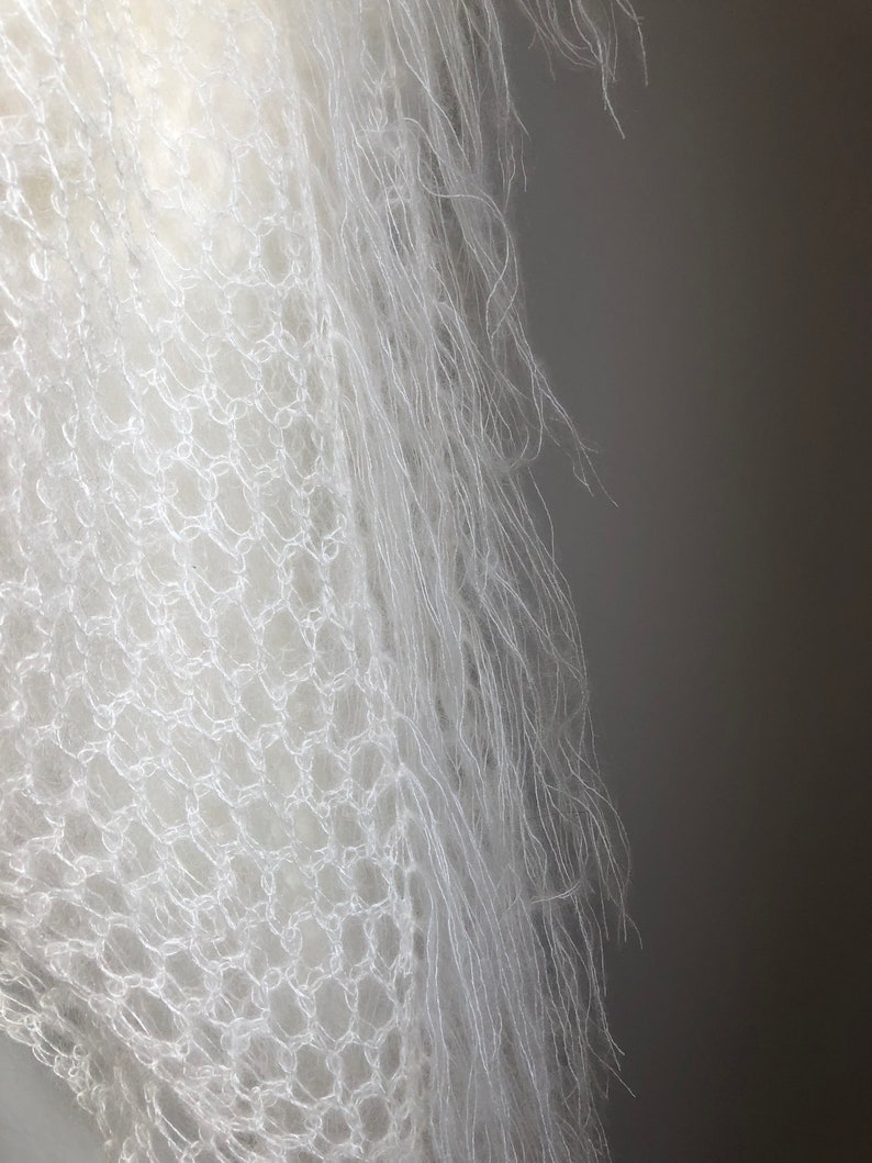 May include: White crocheted shawl with a delicate, lacy pattern and a soft, fluffy texture.