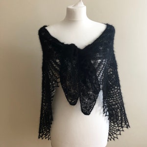 May include: A black lace shawl with a delicate pattern, draped over a white mannequin.