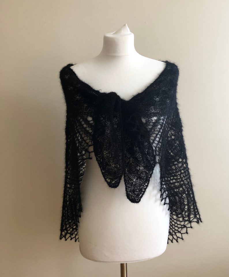 May include: A black lace shawl with a delicate pattern, draped over a white mannequin.
