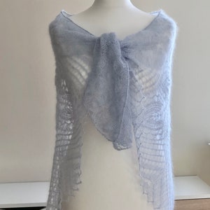 May include: A light blue knitted shawl with a delicate lace pattern. The shawl is draped over a white mannequin.