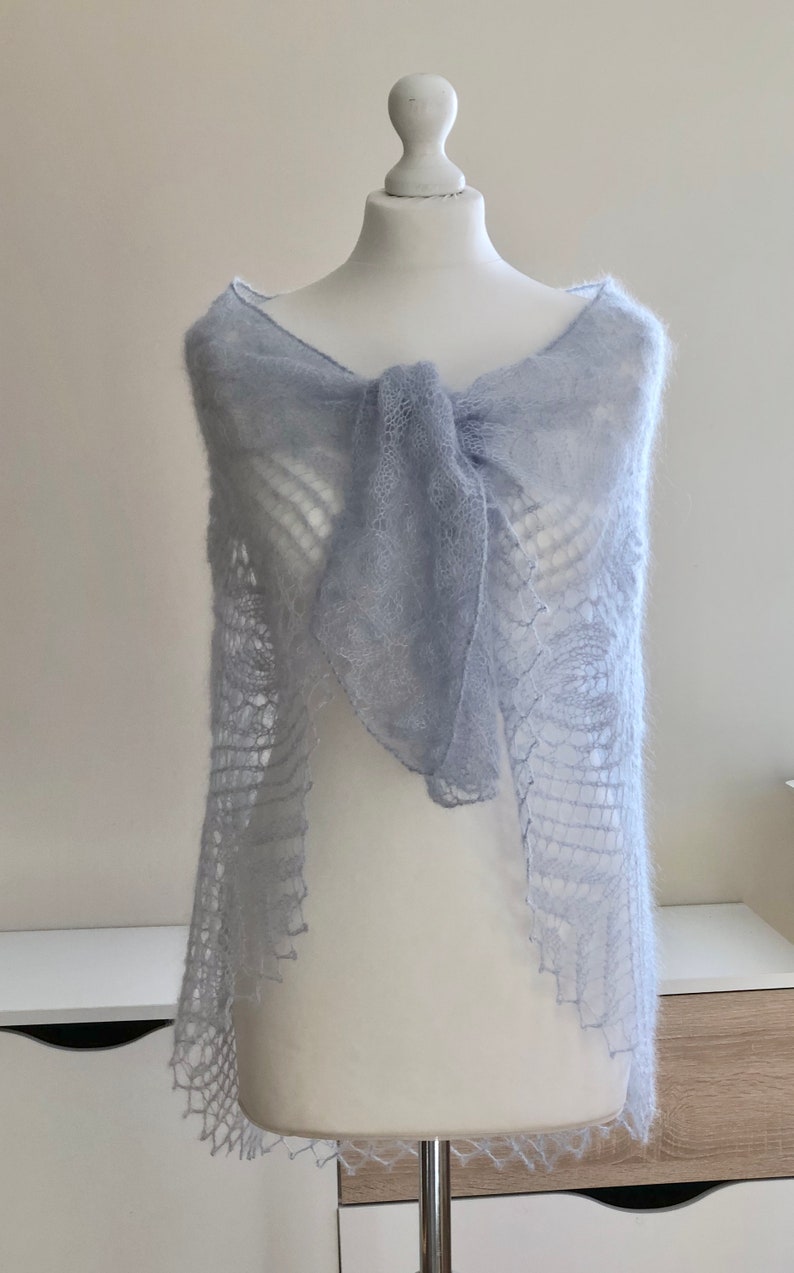 May include: A light blue knitted shawl with a delicate lace pattern. The shawl is draped over a white mannequin.