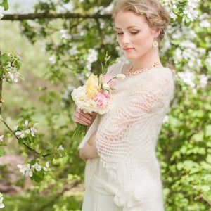 May include: A woman in a white lace shawl holds a bouquet of yellow and pink flowers in front of a blooming tree.