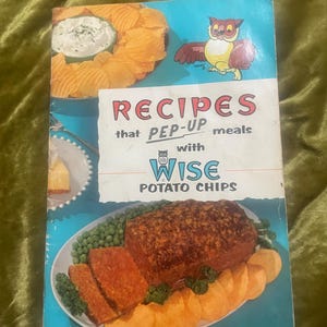 May include: A vintage cookbook titled RECIPES that PEP-UP meals with WISE POTATO CHIPS. The cover features a cartoon owl, a bowl of chips with dip, and a platter of meatloaf with peas and potato chips on a blue background with white text.