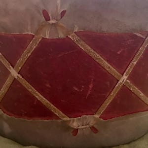 May include: A cylindrical drum featuring a deep red diamond-patterned exterior overlay. The red sections are separated by thin, light-colored, intersecting strips that create a lattice design. The top and bottom edges are finished with a light-colored material.
