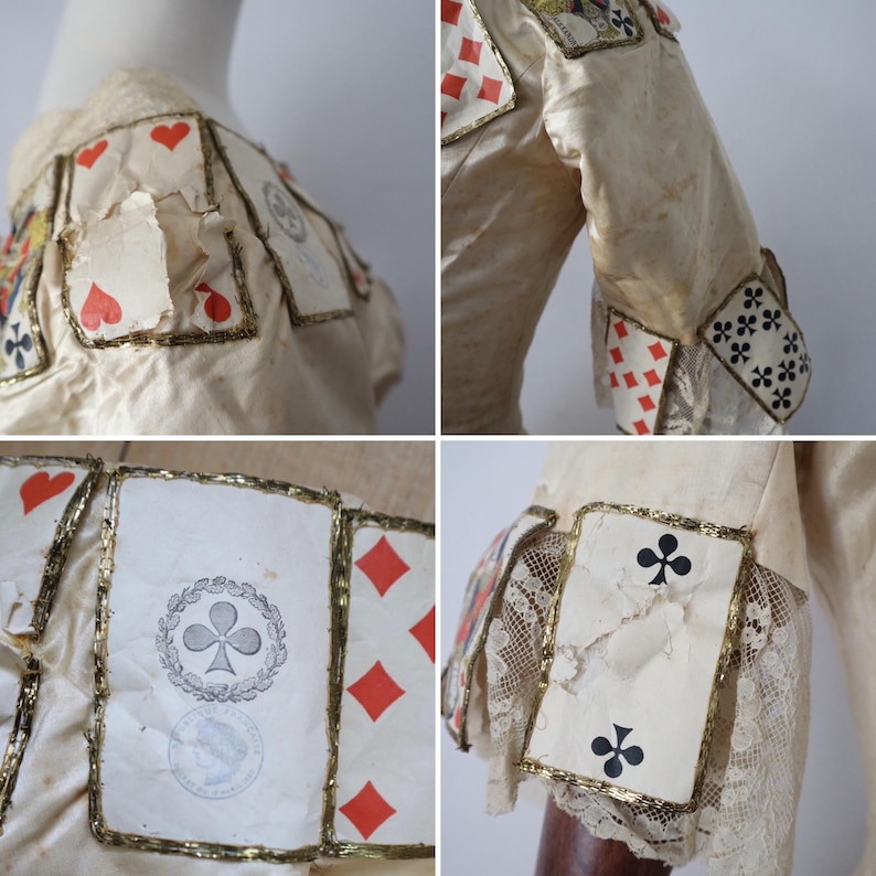 May include: Cream-colored garment adorned with playing card motifs. The cards, featuring hearts, diamonds, clubs, and spades, are outlined with gold trim. The sleeves have lace and card details. The garment appears vintage or antique.