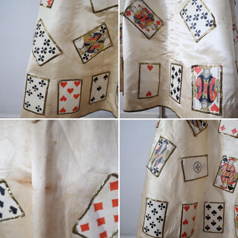 May include: Cream-colored fabric with playing card appliqu&eacute;s. The cards include hearts, spades, clubs, and diamonds, each with gold trim. The fabric appears to be a skirt or dress.