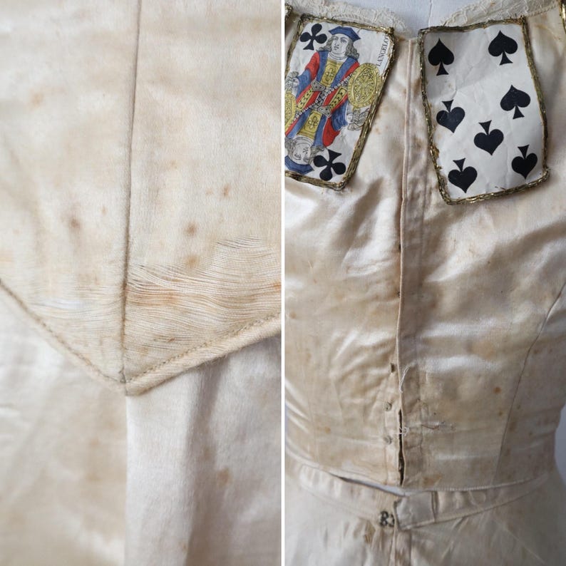 May include: Cream-colored vintage garment with playing card accents. The bodice features a Jack of Clubs and a Seven of Spades card, trimmed with gold. The fabric shows age spots, adding to its antique aesthetic. The garment has a button-down front.