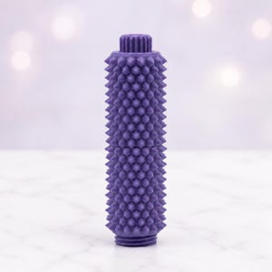 Peut inclure: Un rouleau de massage cylindrique violet doté d'un motif dense et uniforme de petites pointes sur toute sa surface. L'objet présente un capuchon circulaire strié au sommet et une base striée assortie, formant un outil texturé et tactile.