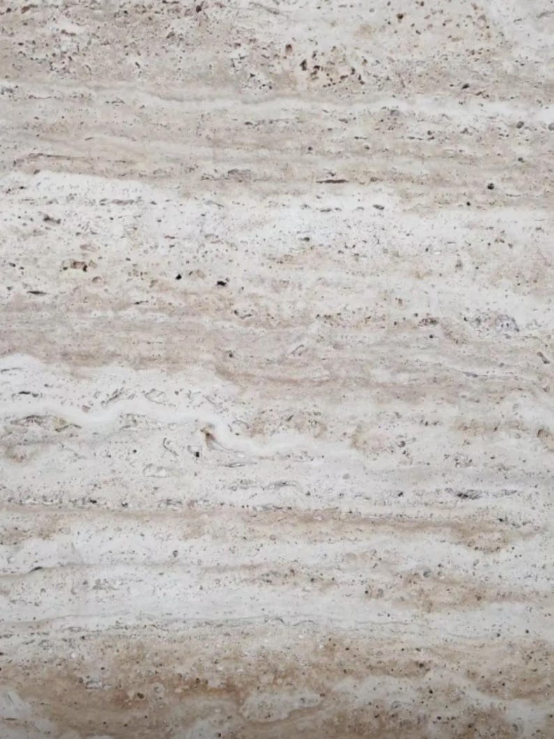 May include: A slab of natural travertine stone featuring a horizontal banded pattern in shades of beige, cream, and light brown. The surface displays a porous, textured appearance with small pits and irregular mineral veins running across the face.