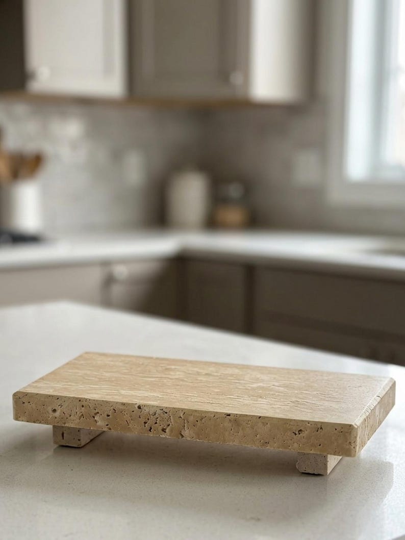 May include: A rectangular beige travertine stone riser with a porous, textured surface and natural veining. The platform is elevated by four small, matching stone feet, providing a stable base for display purposes on a flat surface.