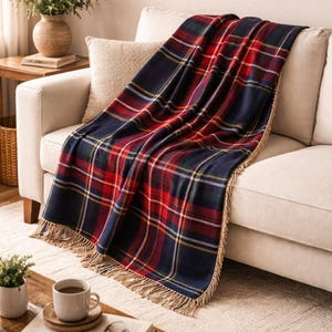May include: A navy blue, red, and yellow plaid throw blanket with a fringed edge is draped over a beige sofa. The blanket's pattern is a classic tartan design, adding a touch of warmth and style to the living room setting.