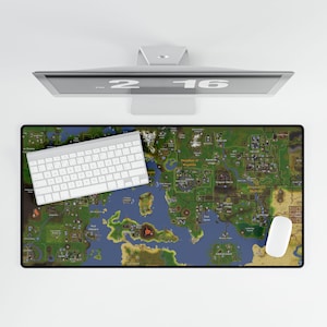 May include: A rectangular desk mat featuring a detailed map design with green, blue, and brown tones. A white keyboard and mouse are positioned on the mat. A computer monitor is above the mat.