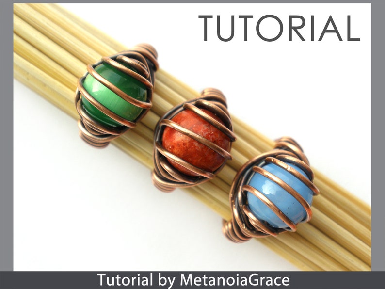 Op de afbeelding: Drie draadgewikkelde ringen met verschillende gekleurde stenen. De ringen zijn gemaakt van koperdraad en hebben groene, oranje en blauwe stenen. De ringen worden gepresenteerd op een houten oppervlak. Tutorial door MetanoiaGrace.