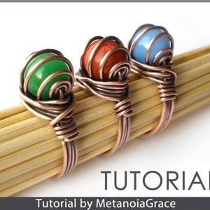 Op de afbeelding: Drie ringen van koperdraad gewikkeld met verschillende gekleurde stenen. De ringen zijn groen, rood en blauw. De ringen liggen op een houten oppervlak. TUTORIAL by MetanoiaGrace.