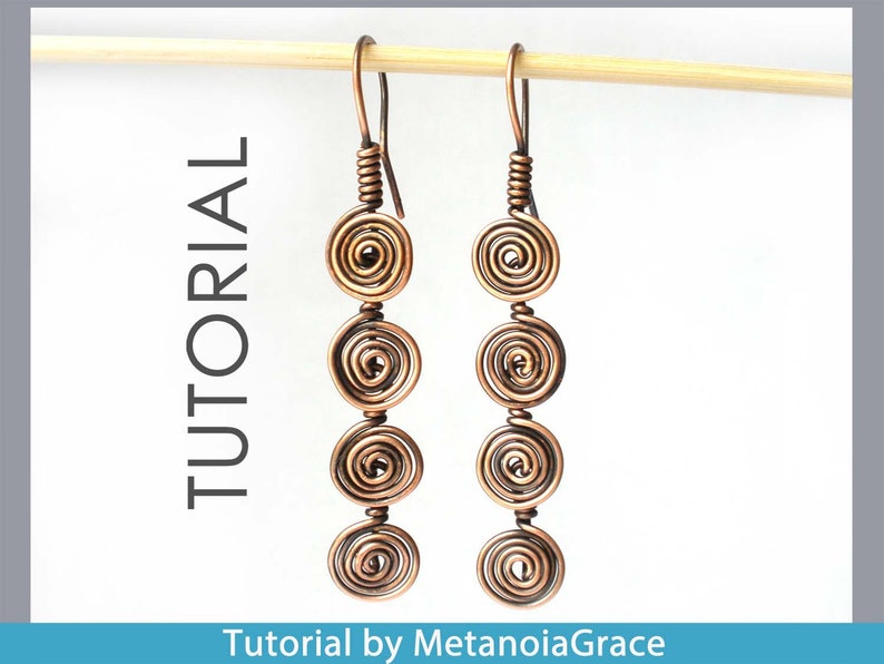 May include: A pair of copper wire earrings with four coiled circles on each earring. The earrings are hanging from a wooden dowel.