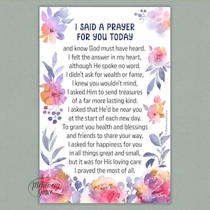 May include: A watercolor print with the text "I Said a Prayer For You Today." The design features floral accents in shades of pink, purple, and orange. The print includes the artist's signature, "Metanoia Grace."