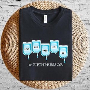 Op de afbeelding: Zwart t-shirt met een afbeelding van vijf IV-zakken met de labels LEVO, NEO, VASO, EPI en JC. De tekst "#FIFTHPRESSOR" staat onder de zakken. Het shirt wordt gepresenteerd op een geweven, cirkelvormig oppervlak.