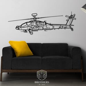 May include: Black metal wall art of an Apache helicopter, with a black couch and yellow throw pillow in the foreground. The art is mounted on a white wall with a black floor lamp in the background.